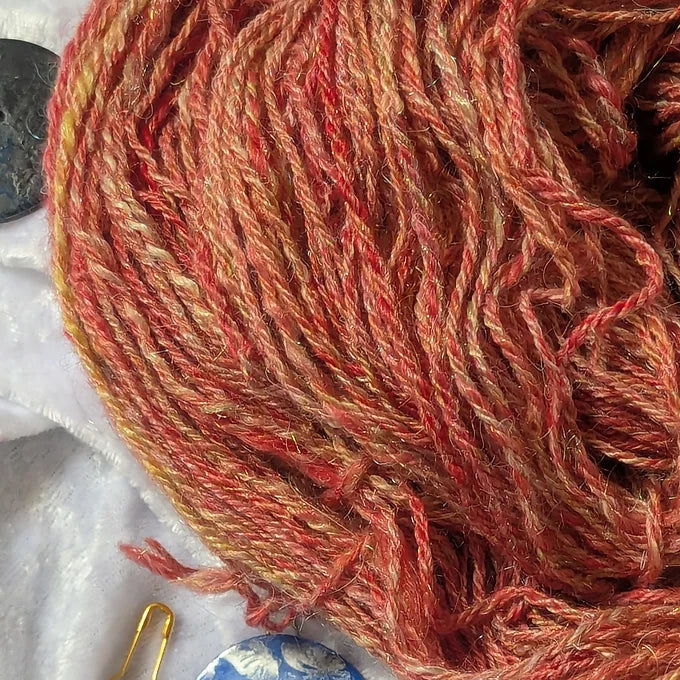 Close-up of red and orange yarn with a hook on a white background